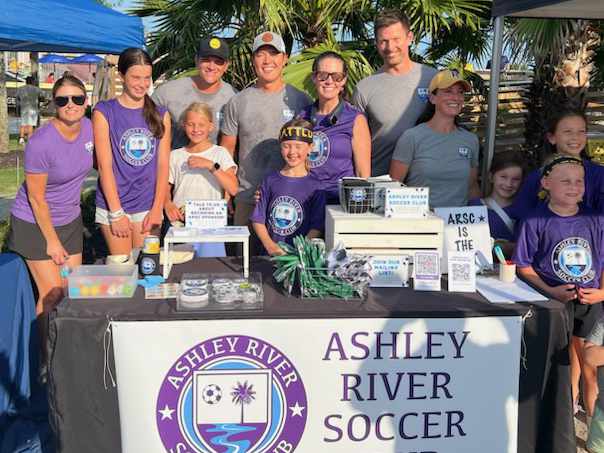 A youth soccer club's parent volunteers and players gathered at their team fundraising table
