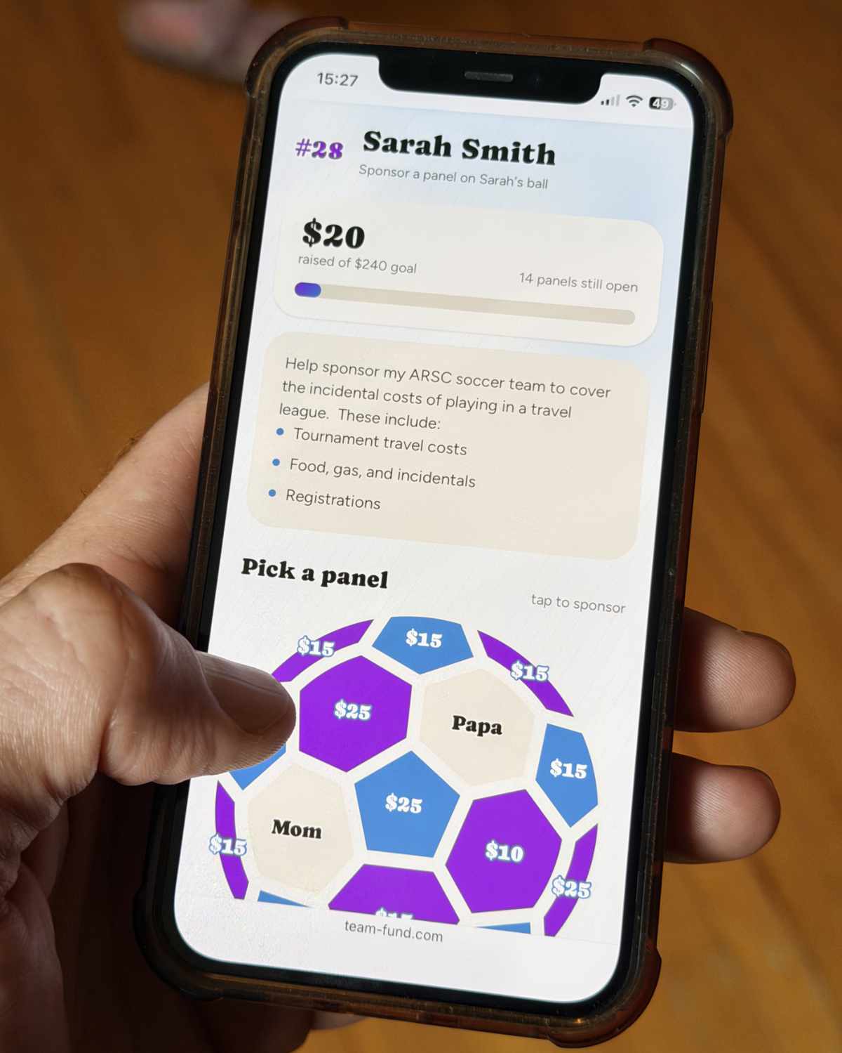 A phone held in a hand, showing a player's sponsorship page with a soccer-ball graphic partway filled in with sponsors' names and panel amounts